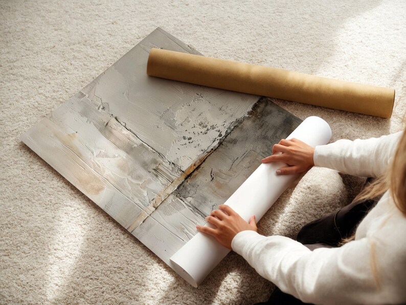 May include: An abstract art print with neutral tones of gray, white, and beige. A rolled-up print and a cardboard tube are next to the artwork. The image is taken from an overhead perspective.