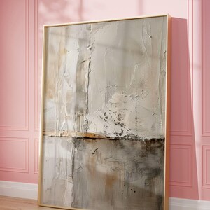 May include: Abstract textured artwork in a gold frame. The painting features a neutral color palette with shades of beige, gray, and brown. The artwork is leaning against a pink wall and wooden floor.