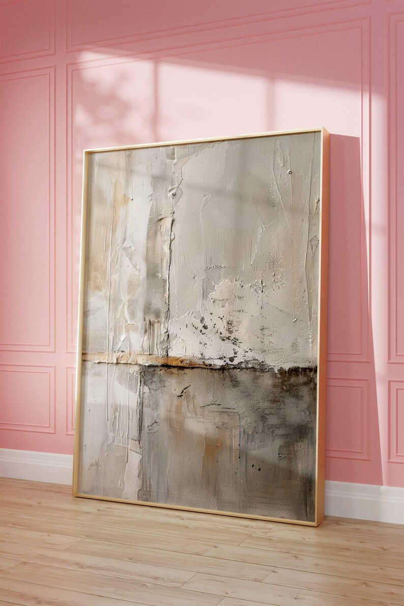May include: Abstract textured artwork in a gold frame. The painting features a neutral color palette with shades of beige, gray, and brown. The artwork is leaning against a pink wall and wooden floor.