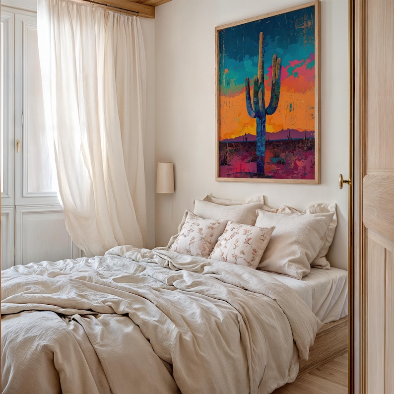 May include: A bedroom with a bed made with a beige linen duvet and pillows. The bed is next to a window with white curtains. A large framed painting of a cactus against a sunset sky hangs on the wall above the bed.