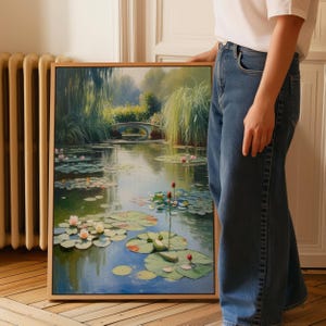 Puede incluir: Pintura enmarcada de una serena escena de estanque con nen&uacute;fares, flores de loto y un peque&ntilde;o puente al fondo. La obra de arte presenta un marco de madera y una paleta de colores suaves de verdes, azules y rosas.