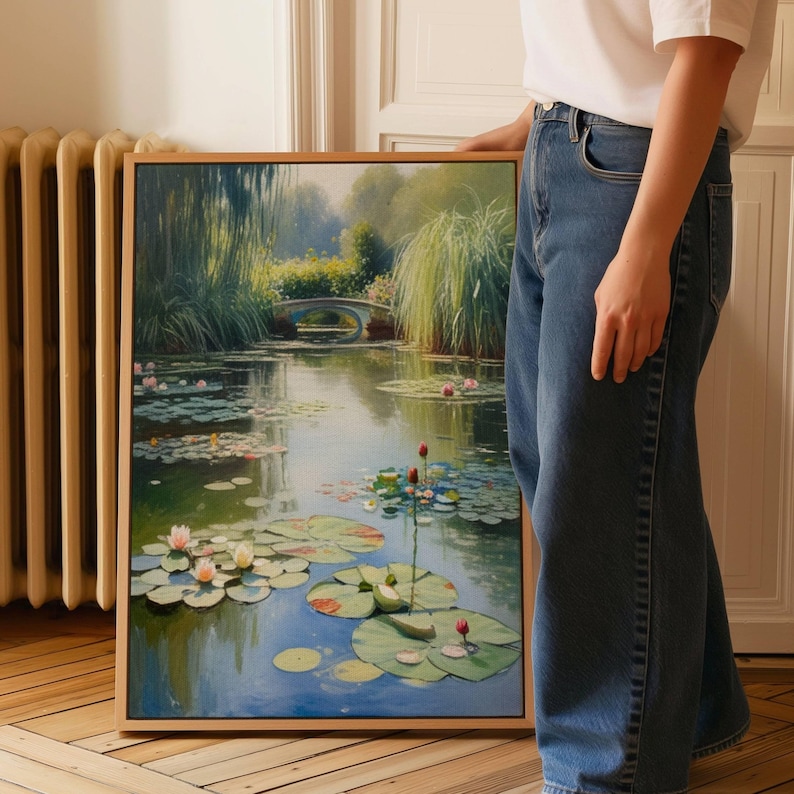 Puede incluir: Pintura enmarcada de una serena escena de estanque con nen&uacute;fares, flores de loto y un peque&ntilde;o puente al fondo. La obra de arte presenta un marco de madera y una paleta de colores suaves de verdes, azules y rosas.