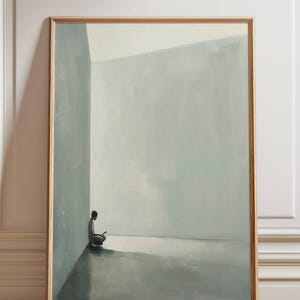 May include: A framed art print featuring a minimalist painting. The artwork depicts a solitary figure seated in a corner of a room, rendered in muted shades of gray and blue. The wooden frame adds a touch of warmth to the serene scene.
