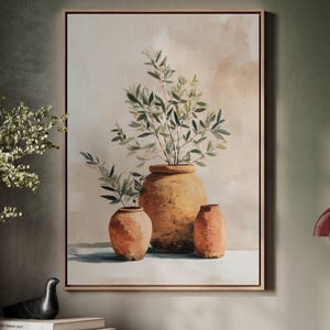 May include: A framed canvas art print featuring three terracotta-colored vases, each with a unique shape, holding green leafy branches. The background has soft beige and peach tones, and the frame is a light brown.