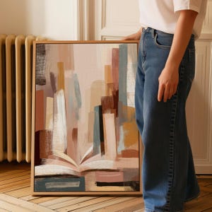 May include: Abstract art print in a wooden frame. The artwork features a layered composition of vertical and horizontal brushstrokes in muted tones of beige, brown, and blue. The painting evokes the form of an open book.