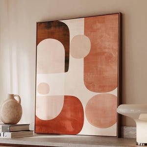 May include: Abstract art print featuring a geometric design in shades of red, pink, and brown. The artwork is framed in a dark brown wooden frame. The shapes include circles and rounded rectangles. The art is displayed on a wooden cabinet.