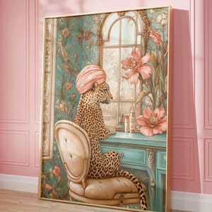 May include: A framed art print featuring a leopard wearing a pink turban, seated at a teal vanity. The leopard is in a room with floral wallpaper and a window. The artwork has a gold frame and a vintage aesthetic.
