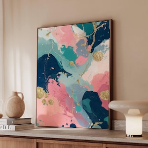 May include: Abstract art print with a wooden frame. The artwork features a blend of pink, teal, navy, and gold colors. The design includes brushstrokes and splatters, creating a modern and artistic aesthetic. The print is displayed on a wooden cabinet.