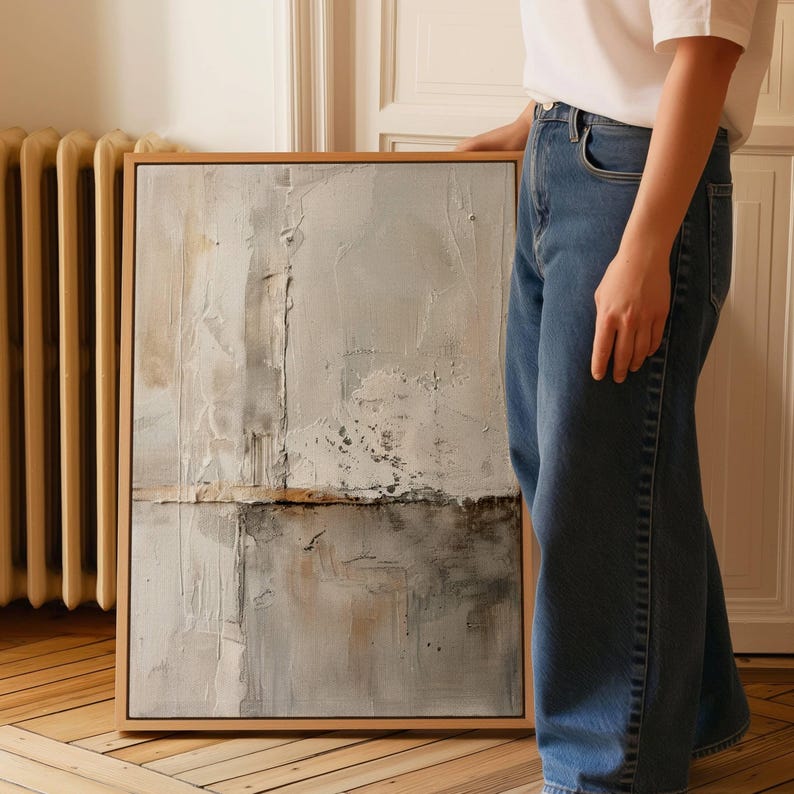 May include: Abstract art piece in a wooden frame. The artwork features a textured surface with a palette of gray, white, and brown tones. The composition includes vertical and horizontal elements, creating a layered effect. The artwork is displayed indoors.