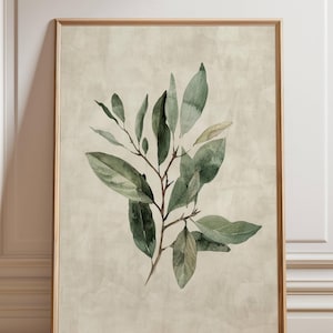 May include: A framed botanical print featuring a watercolor illustration of a leafy branch. The leaves are various shades of green, with a brown stem, set against a beige background. The frame is a light brown color.
