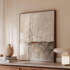 May include: Abstract art piece in a wooden frame. The artwork features a textured, neutral color palette with shades of beige, gray, and brown. The composition is divided horizontally, with a lighter upper section and a darker lower section.