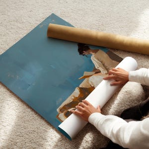 May include: An abstract art print with a blue background and a figure in white clothing. A rolled-up white canvas and a brown cardboard tube are next to the artwork. The image is on a light-colored carpet.
