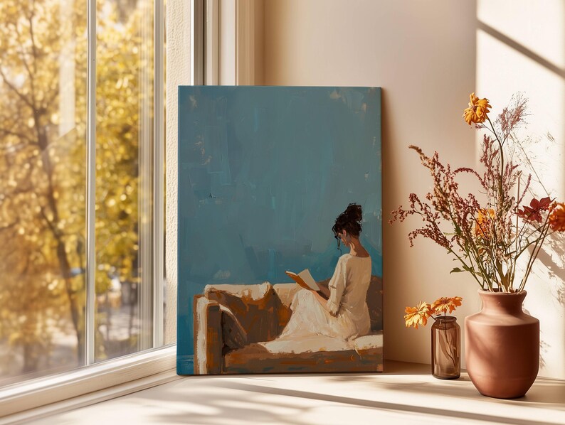 May include: An oil painting depicts a person reading on a sofa, set against a teal background. The artwork is displayed near a window with a view of fall foliage. A vase of dried flowers and a small glass jar with flowers are on a white surface.