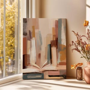 May include: An abstract canvas print featuring a book with open pages, painted in shades of beige, brown, and blue. The artwork is displayed near a window with a view of a tree with yellow leaves, and a vase of dried flowers.