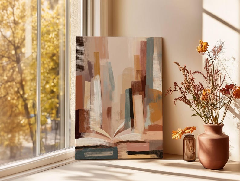 May include: An abstract canvas print featuring a book with open pages, painted in shades of beige, brown, and blue. The artwork is displayed near a window with a view of a tree with yellow leaves, and a vase of dried flowers.