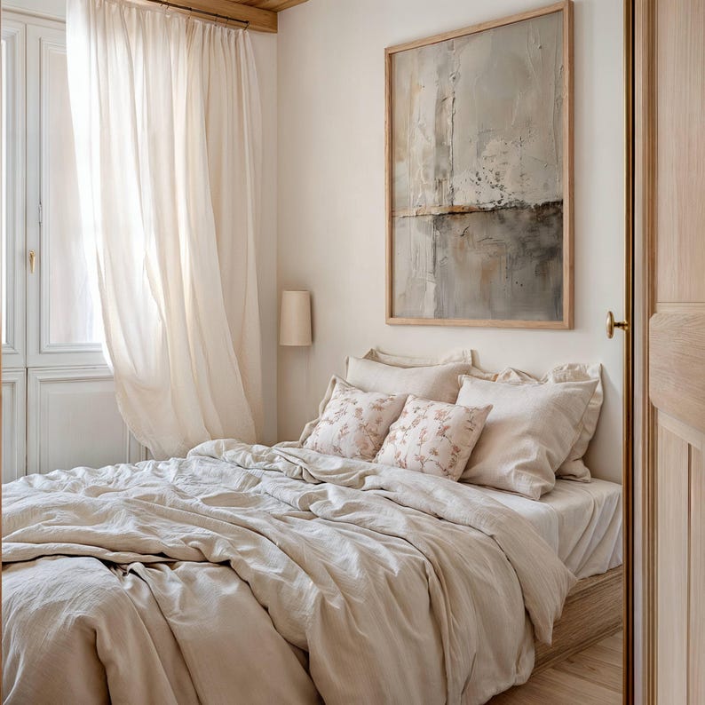 May include: A bedroom scene featuring a bed with beige bedding and decorative pillows with floral patterns. A large framed abstract painting hangs above the bed. Sheer curtains frame a window, and a wall-mounted lamp is visible.