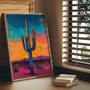 May include: A framed abstract painting of a large, blue-green cactus with a colorful sunset background. The cactus is in the center of the painting and is surrounded by a desert landscape.