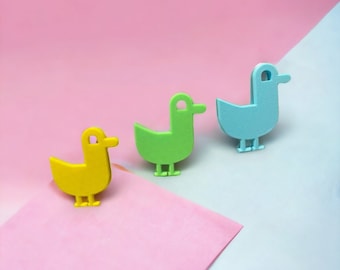 Puede incluir: Tres patos de juguete en fila sobre un fondo rosa y azul. Los patos son amarillos, verdes y azules.