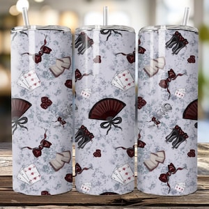 Può includere: Tre bicchieri in acciaio inossidabile con un motivo ripetuto di carte da gioco, ventagli, fiocchi e corsetti in bordeaux e nero su sfondo grigio chiaro. Ogni bicchiere ha un coperchio argentato e una cannuccia trasparente.