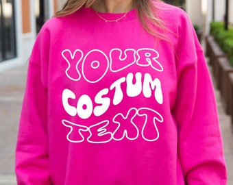 May include: A bright pink sweatshirt with white text that reads "YOUR COSTUM TEXT" in a retro, bubble-letter font.