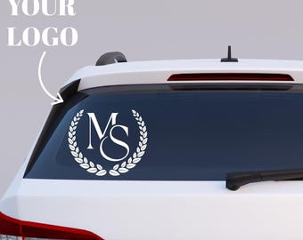 May include: A white vinyl decal applied to the rear window of a white vehicle. The decal features the letters MS in a serif font, enclosed within a circular laurel wreath design. The text YOUR LOGO with an arrow pointing to the decal is visible.