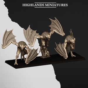 Peut inclure: Trois créatures miniatures en forme de chauve-souris avec des ailes déployées, posées sur une base noire. Les créatures ont des fourrures détaillées et des dents pointues, avec le texte "HIGHLANDS MINIATURES" au-dessus. Les figurines sont de couleur marron clair.