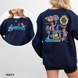 Puede incluir: Sudadera azul marino con la palabra "Zootopia" bordada en turquesa en la parte delantera. La parte trasera muestra un gr&aacute;fico colorido de personajes de la pel&iacute;cula animada "Zootopia".