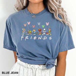K&ouml;nnte beinhalten: Blaues Jeans-T-Shirt mit einer Grafik von Zeichentrickfiguren, die Mickey Mouse-f&ouml;rmige Ballons &uuml;ber dem Wort "FRIENDS" in Wei&szlig; halten. Das Shirt hat einen Rundhalsausschnitt und kurze &Auml;rmel.