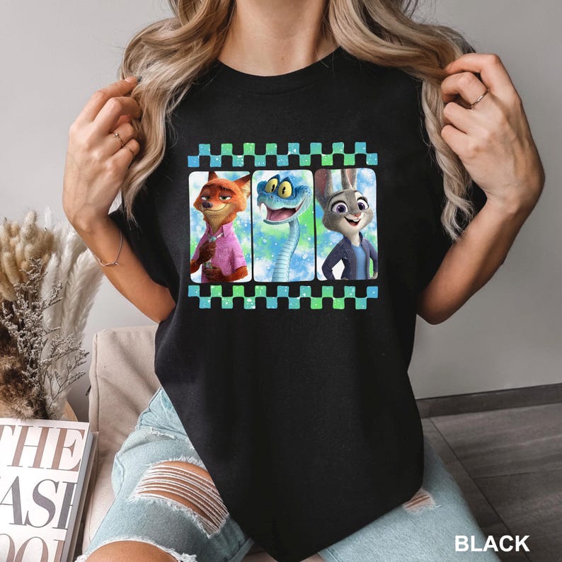 May include: Black crew neck t-shirt featuring a colorful graphic of three animated characters: a fox, a snake, and a rabbit. The graphic is framed by a green and blue checkered border. The word "BLACK" is printed at the bottom.
