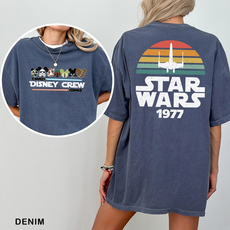 May include: Denim blue t-shirt with a Disney Crew graphic on the front and a Star Wars design on the back. The Star Wars design includes a retro sunset, a spaceship, and the text "STAR WARS 1977".