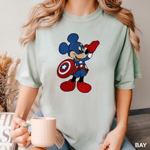 a woman holding a cup of coffee and wearing a mickey mouse t - shirt