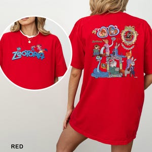 以下が含まれることがあります： 青色の「Zootopia」の文字が入った赤いTシャツ。前面と背面に漫画のキャラクターが描かれています。Tシャツの背面には、さまざまなキャラクターがフレームに入ったデザインが施されています。シャツは鮮やかな赤色です。