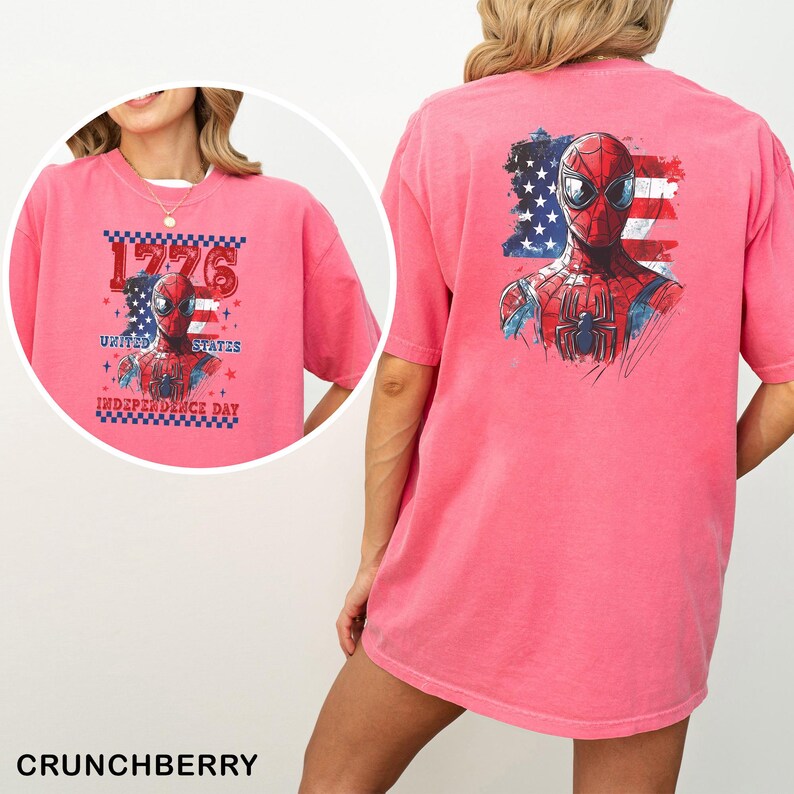 May include: A pink t-shirt featuring a graphic of Spider-Man in front of an American flag. The back displays a large Spider-Man illustration. The front shows the text 1776 UNITED STATES INDEPENDENCE DAY with a checkered border and Spider-Man graphic.