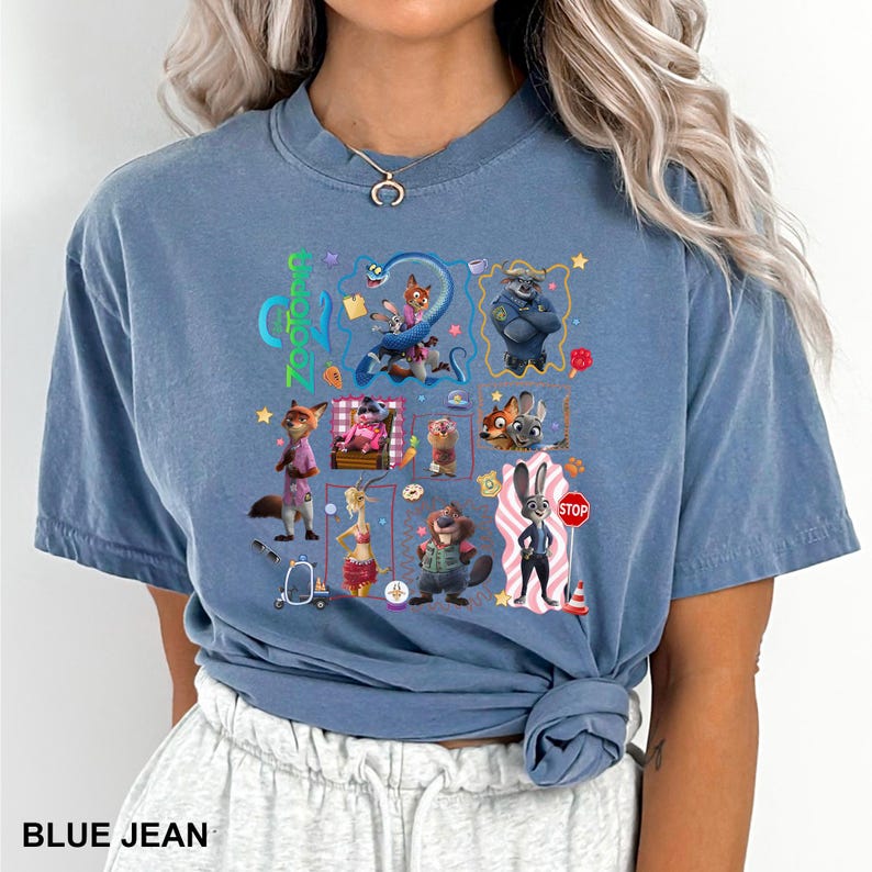 May include: A blue jean colored t-shirt featuring a graphic print of various Zootopia characters including Judy Hopps and Nick Wilde. The design includes multiple small illustrations of the movie cast, colorful icons, and the Zootopia logo text.