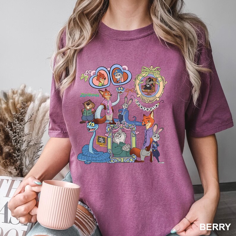 May include: A berry-colored short-sleeve t-shirt featuring a graphic print of various animated characters from Zootopia, including Nick Wilde and Judy Hopps, arranged within decorative frames and heart shapes with the text Zootopia printed below.