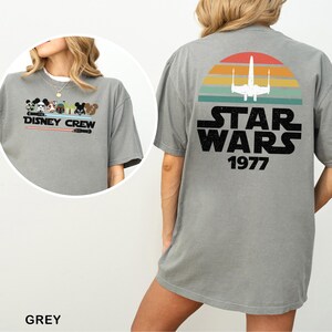 May include: A grey t-shirt with a Disney Crew graphic on the front and a Star Wars design on the back. The Star Wars design features a retro sunset, a spaceship, and the text "STAR WARS 1977".
