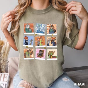 May include: Khaki-colored t-shirt featuring a grid of cartoon character portraits in polaroid-style frames. The portraits showcase various animal characters in different outfits and settings, with a star graphic at the bottom of each frame. The word "KHAKI" is printed at the bottom right.