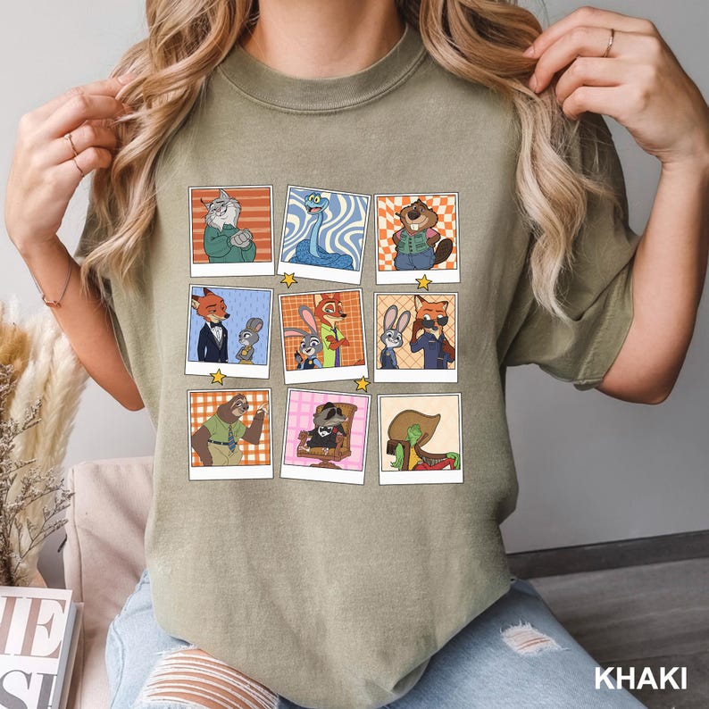 May include: Khaki-colored t-shirt featuring a grid of cartoon character portraits in polaroid-style frames. The portraits showcase various animal characters in different outfits and settings, with a star graphic at the bottom of each frame. The word "KHAKI" is printed at the bottom right.