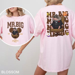 May include: Pale pink t-shirt with a cartoon image of Mr. Big from Zootopia. The front design has the text "MR. BIG" and the back design shows Mr. Big in a chair with text. The shirt is a blossom colour.