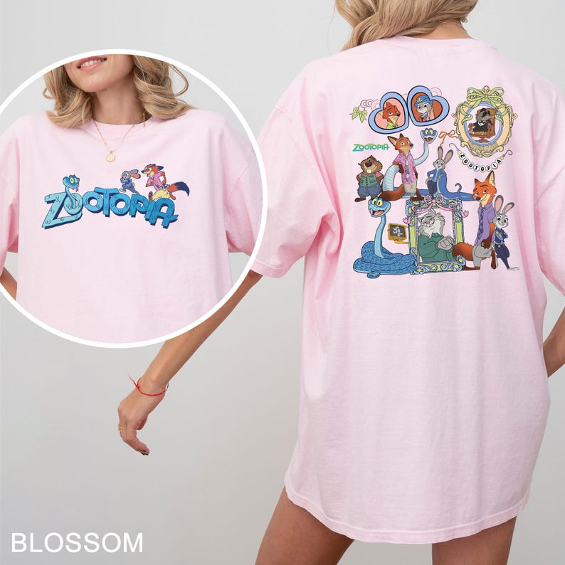 以下が含まれることがあります： 前面に青と緑で「Zootopia」の文字が入った薄いピンク色のTシャツ。Tシャツの背面には、アニメ映画「ズートピア」のキャラクターのカラフルなグラフィックがあります。