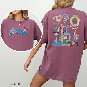 以下が含まれることがあります： 前面に青と緑で「Zootopia」の文字が入ったベリー色のTシャツ。Tシャツの背面には、アニメ映画「Zootopia」のキャラクターのカラフルなグラフィックが表示されています。