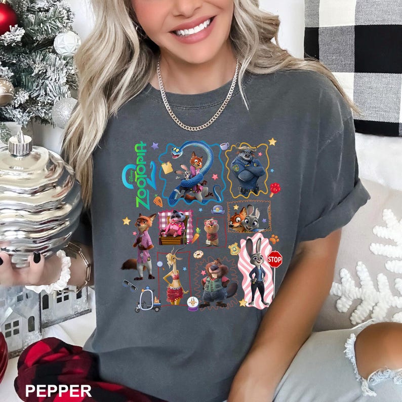 May include: A charcoal gray short-sleeve t-shirt featuring a colorful graphic print of various Zootopia characters, including Nick Wilde and Judy Hopps, arranged in a collage style with small icons like a carrot, a stop sign, and a scooter.
