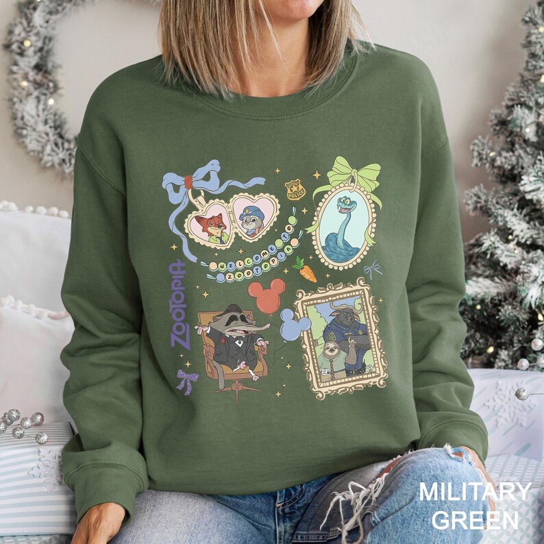 以下が含まれることがあります： Zootopiaのキャラクターが額縁とハート型のロケットに入った、ミリタリーグリーンのスウェットシャツ。デザインにはニック・ワイルド、ジュディ・ホップス、その他のキャラクターが含まれています。「Zootopia」の文字が紫で縦書きされています。