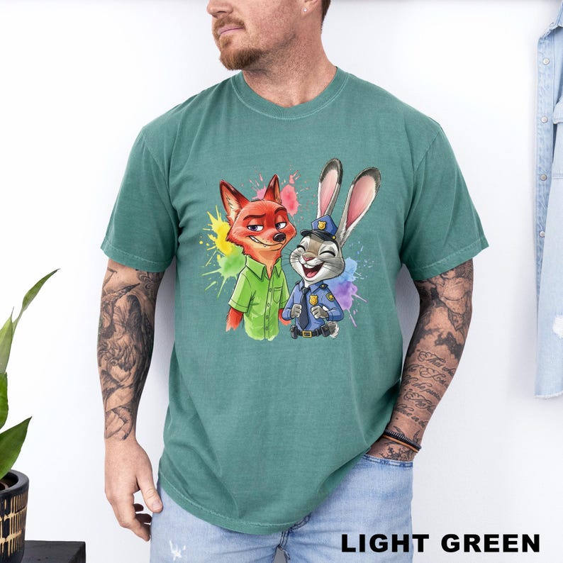 May include: Light green t-shirt featuring a colorful graphic of a fox and a rabbit, both smiling. The fox is wearing a green shirt, and the rabbit is in a police uniform. The words "LIGHT GREEN" are at the bottom of the shirt.