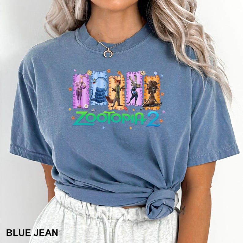 K&ouml;nnte beinhalten: Blaues Jeans-T-Shirt mit dem Text "Zootopia 2" und farbenfrohen Charakterillustrationen. Das Shirt hat einen Rundhalsausschnitt und kurze &Auml;rmel. Der Saum des Shirts ist geknotet.
