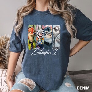 Peut inclure: T-shirt bleu denim avec un graphisme color&eacute; des personnages du film "Zootopie 2". Le graphisme comprend Nick Wilde, Judy Hopps, le chef Bogo et Flash. Les mots "Zootopia 2" sont &eacute;crits en cursive en dessous.