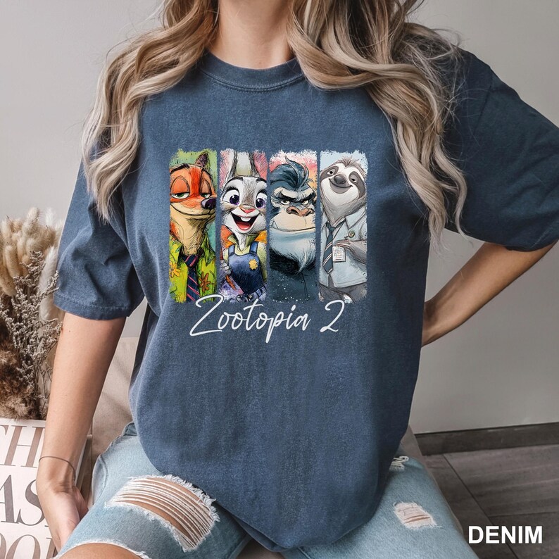 Peut inclure: T-shirt bleu denim avec un graphisme color&eacute; des personnages du film "Zootopie 2". Le graphisme comprend Nick Wilde, Judy Hopps, le chef Bogo et Flash. Les mots "Zootopia 2" sont &eacute;crits en cursive en dessous.