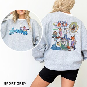 Puede incluir: Sudadera gris deportiva con la palabra "Zootopia" en azul y un gr&aacute;fico de dibujos animados en la parte delantera. La parte trasera de la sudadera tiene un gr&aacute;fico colorido de personajes de la pel&iacute;cula "Zootopia".