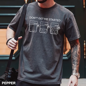 May include: Dark gray t-shirt with the text "DON'T GET ME STARTED" above three jar illustrations. The jars have different contents. The word "PEPPER" is at the bottom of the image.