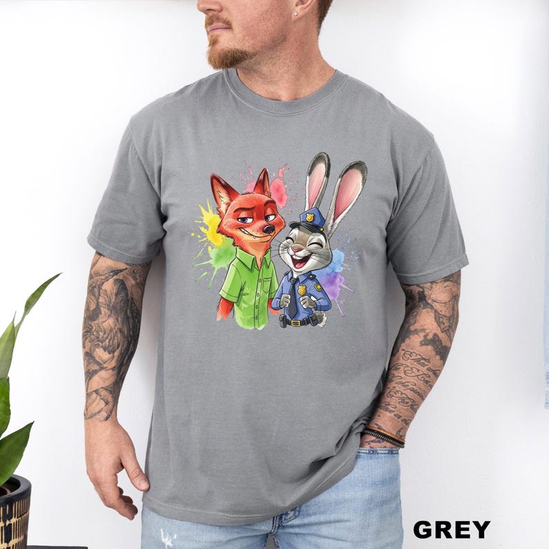 May include: Grey t-shirt featuring a colorful graphic of Nick Wilde the fox and Judy Hopps the rabbit from Zootopia. Nick is wearing a green shirt, and Judy is in a police uniform. The word "GREY" is printed in the bottom right corner.